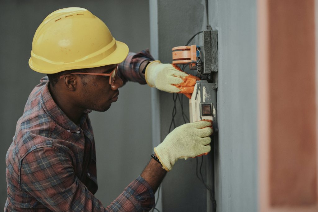 A electrician worker installing a voltaic on a wall wearing gloves and a hardhat helmet