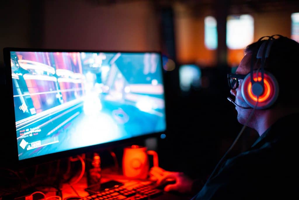 A man playing video games in front of a monitor while wearing a headset