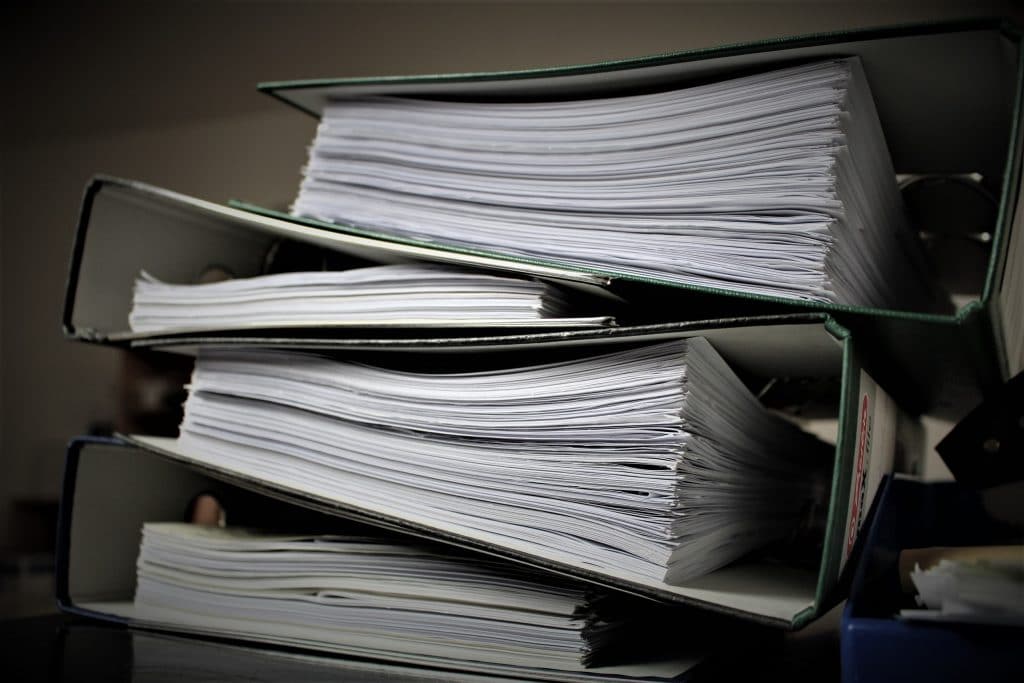 A stack of 3 ring oversized binders filled with documents in a office